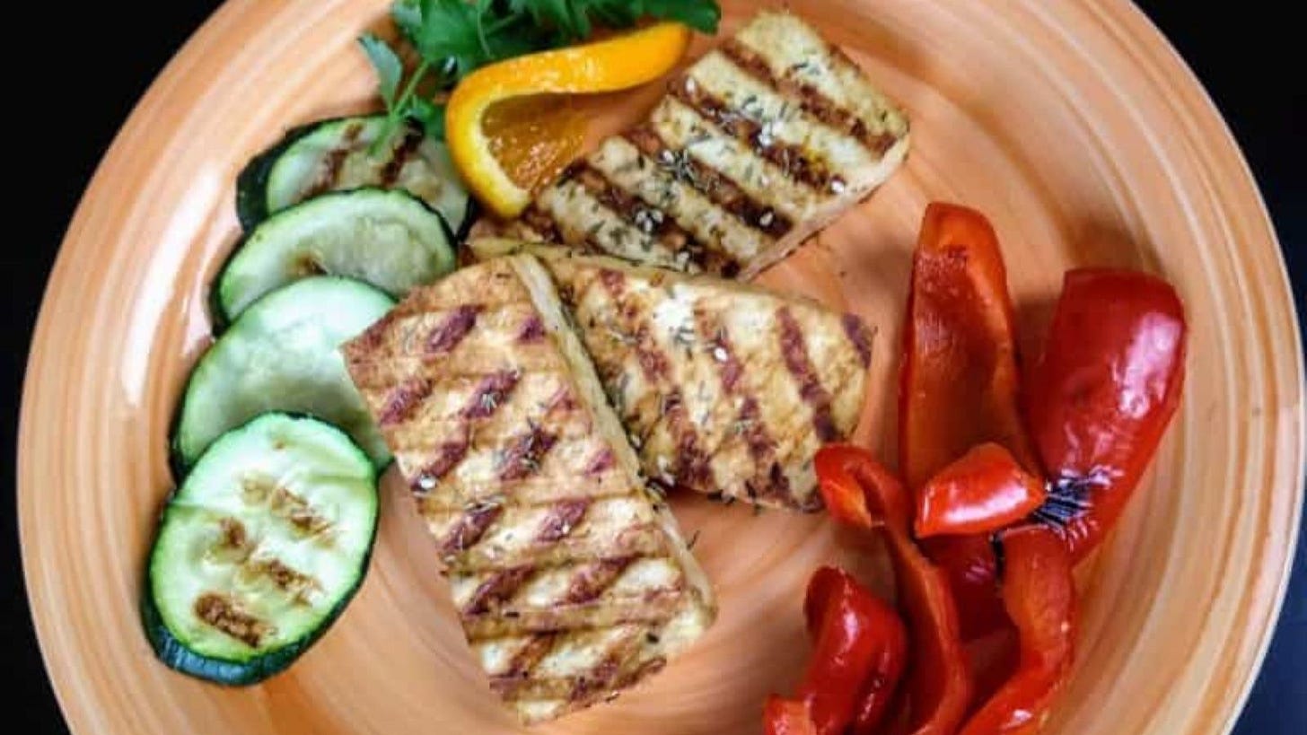 orange tahini grilled tofu on plate with grilled peppers and zucchini.