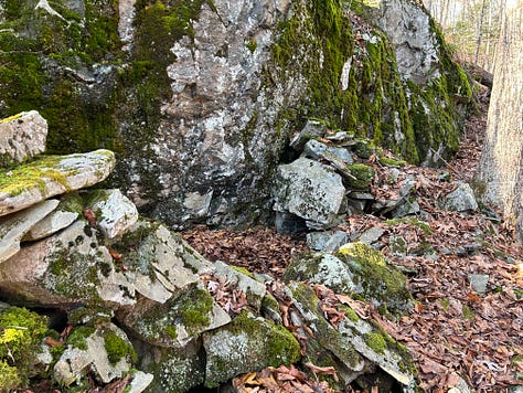 A stone construction in the woods against a cliffside.