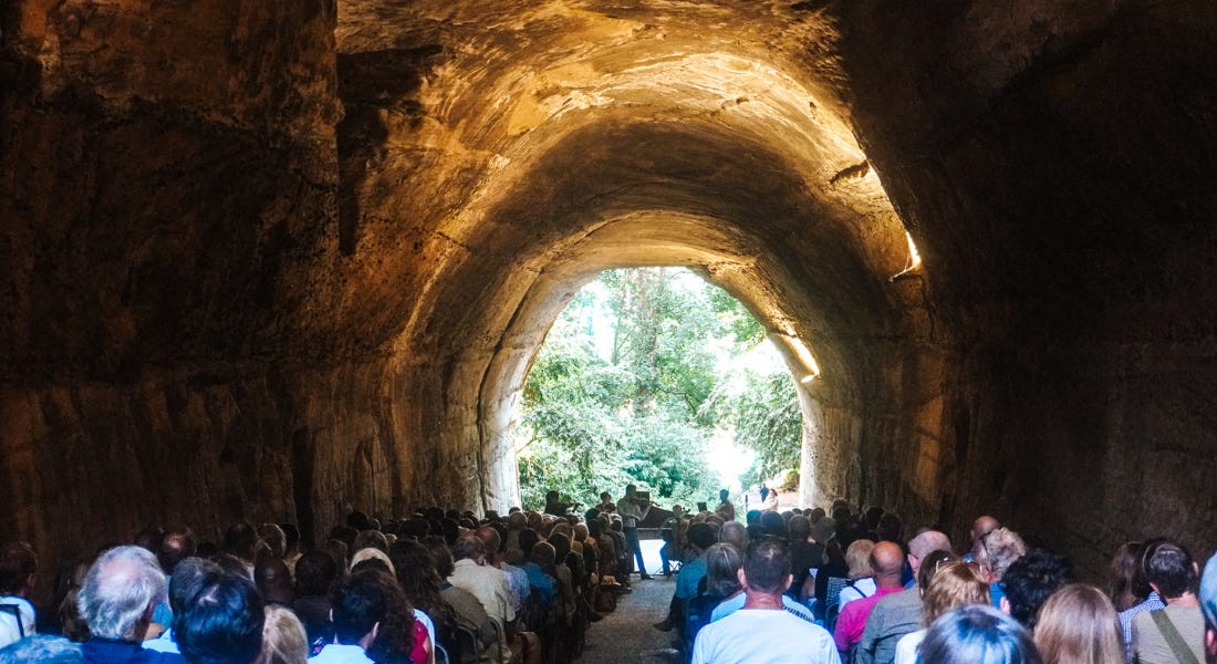 A cave tunnel with a crowd of people sat down and lights around them A cave tunnel with a crowd of people sat down and lights around them