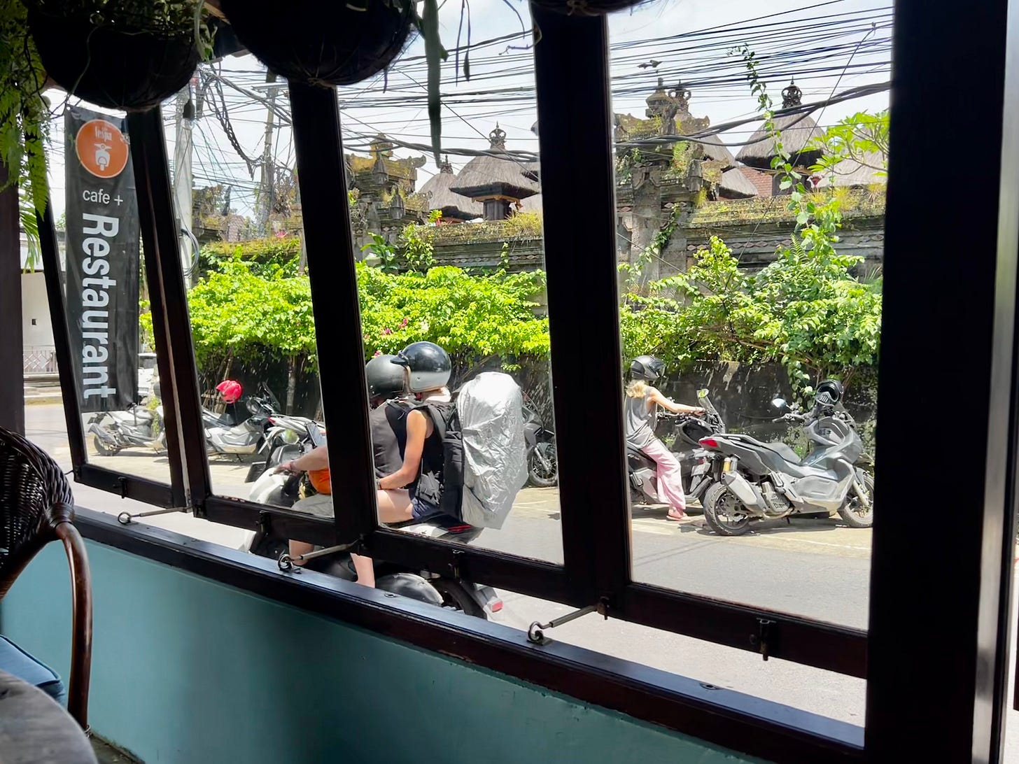 Motorbikes passing on a Bali street, seen through a restaurant window.