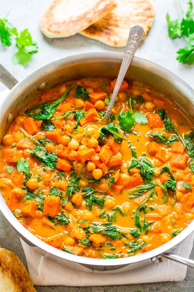 A pot of chickpea and sweet potato curry with a spoon sticking out. 