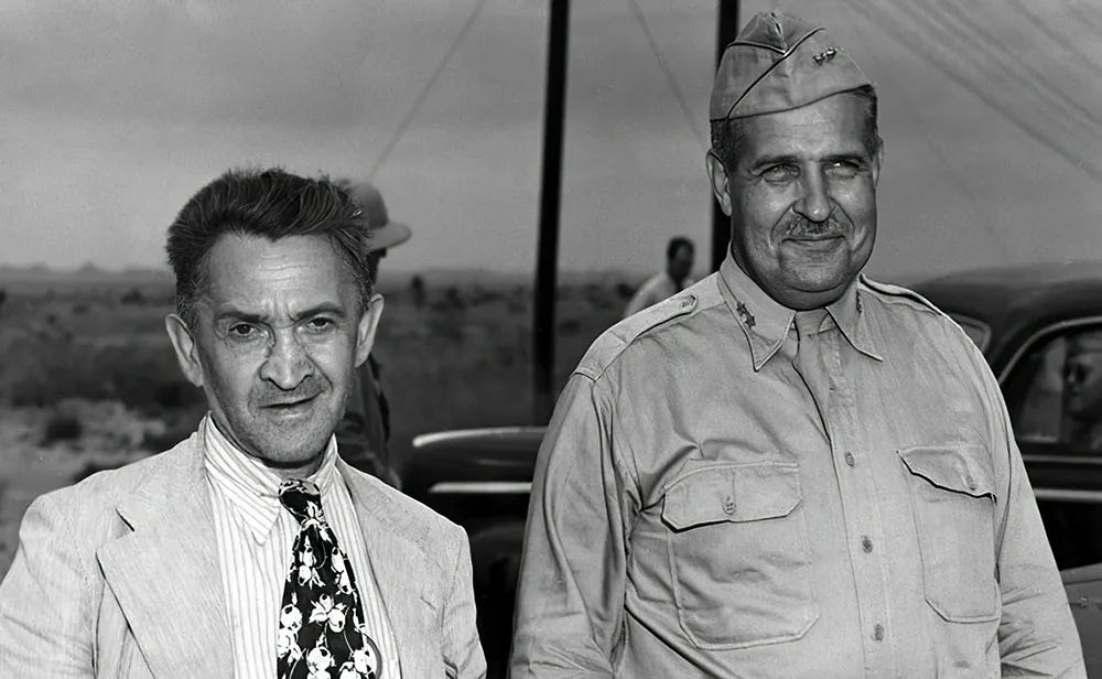 This black-and-white photo shows two men, the shorter one in a suit and patterned tie, and the taller one in a military uniform and cap. A desert landscape with sparse plants is visible in the background. This black-and-white photo shows two men, the shorter one in a suit and patterned tie, and the taller one in a military uniform and cap. A desert landscape with sparse plants is visible in the background.