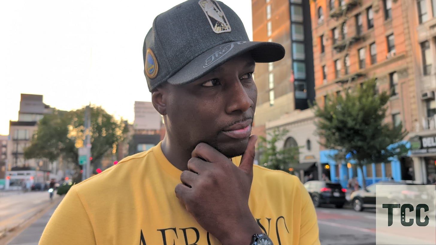 A man stands on a New York City street in golden hour light, wearing a yellow "AERO NYC" shirt and a dark baseball cap adorned with patches. He poses with a thoughtful expression, hand on chin, revealing a Formex Reef watch on his wrist. The background shows blurred cars, brick buildings, and soft reflections of sunset on the cityscape.