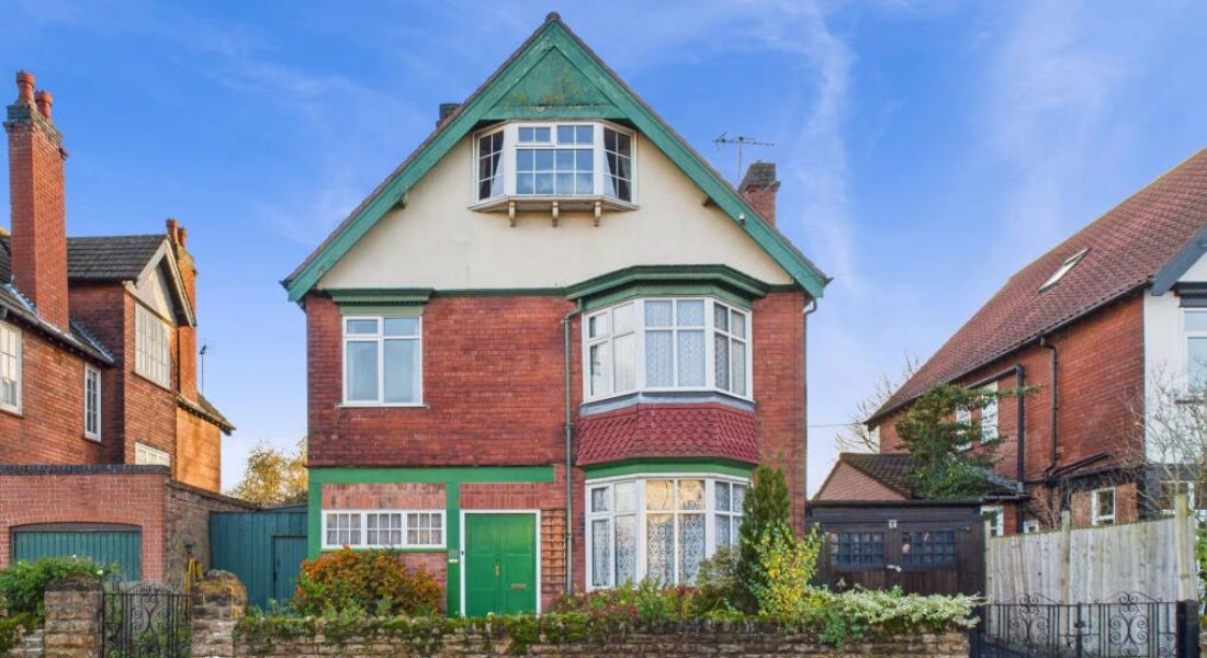 A house with a green, white, and brick exterior, with a brick fence in front of it