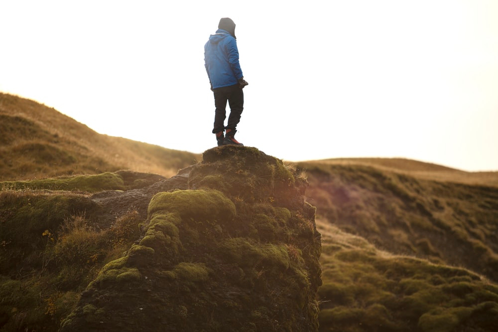 person standing on high ground under white sky person standing on high ground under white sky