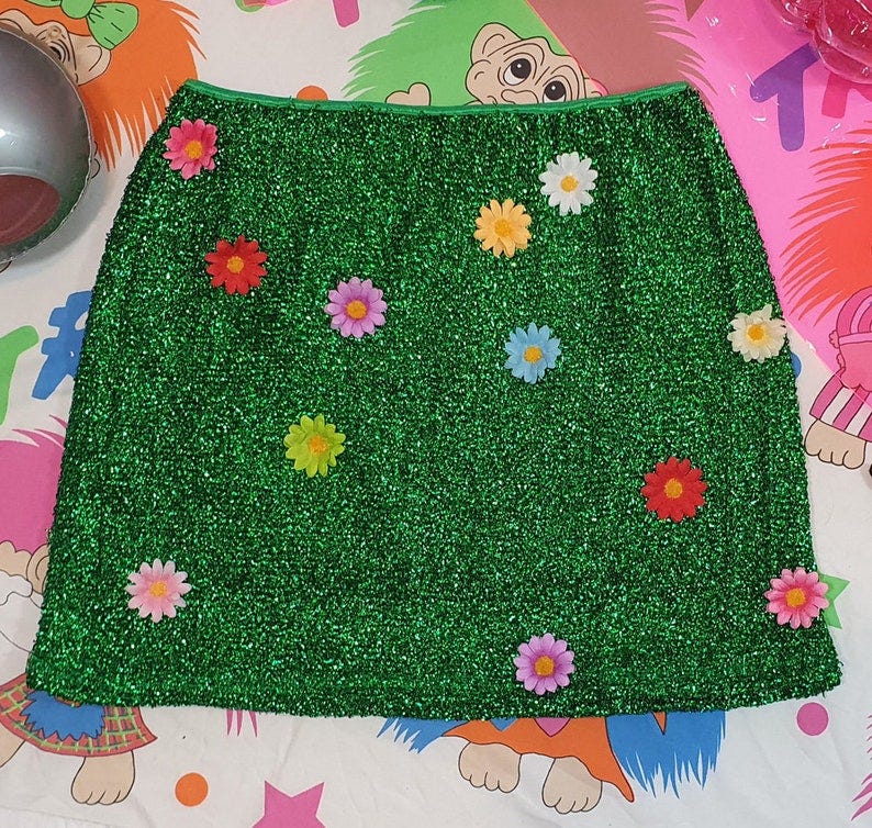 May include: A green sparkly mini skirt with colorful flower embellishments.