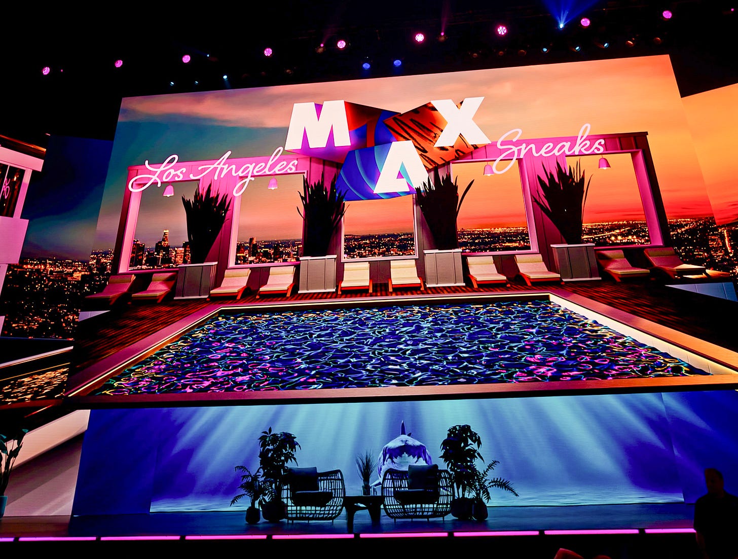 Stage setup at Adobe MAX Sneaks in Los Angeles featuring a rooftop pool–themed design, neon “MAX” signage, and a live audience under colorful lighting.