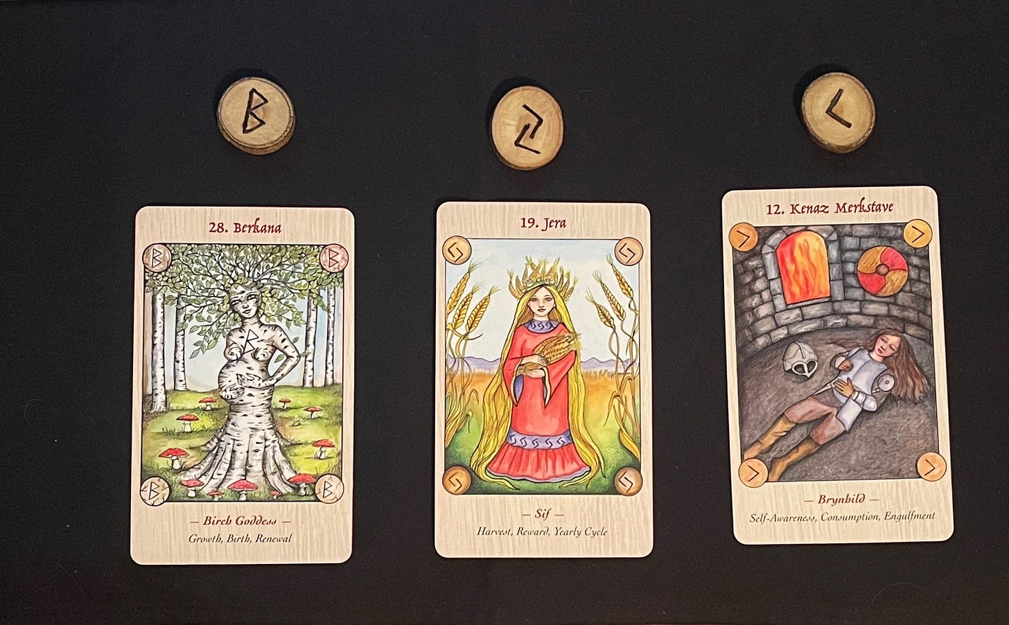 image of wood discs with rune letters inscribed and cards with berkana birch goddess; jera - sif; kenaz - merkstave brynhild