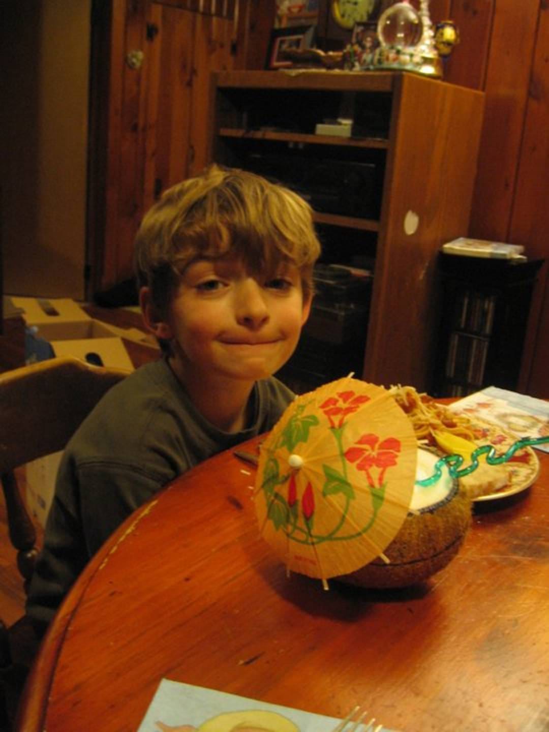 A small boy with a poignant expression on his face enjoying a drink in a coconut with an umbrella in it.