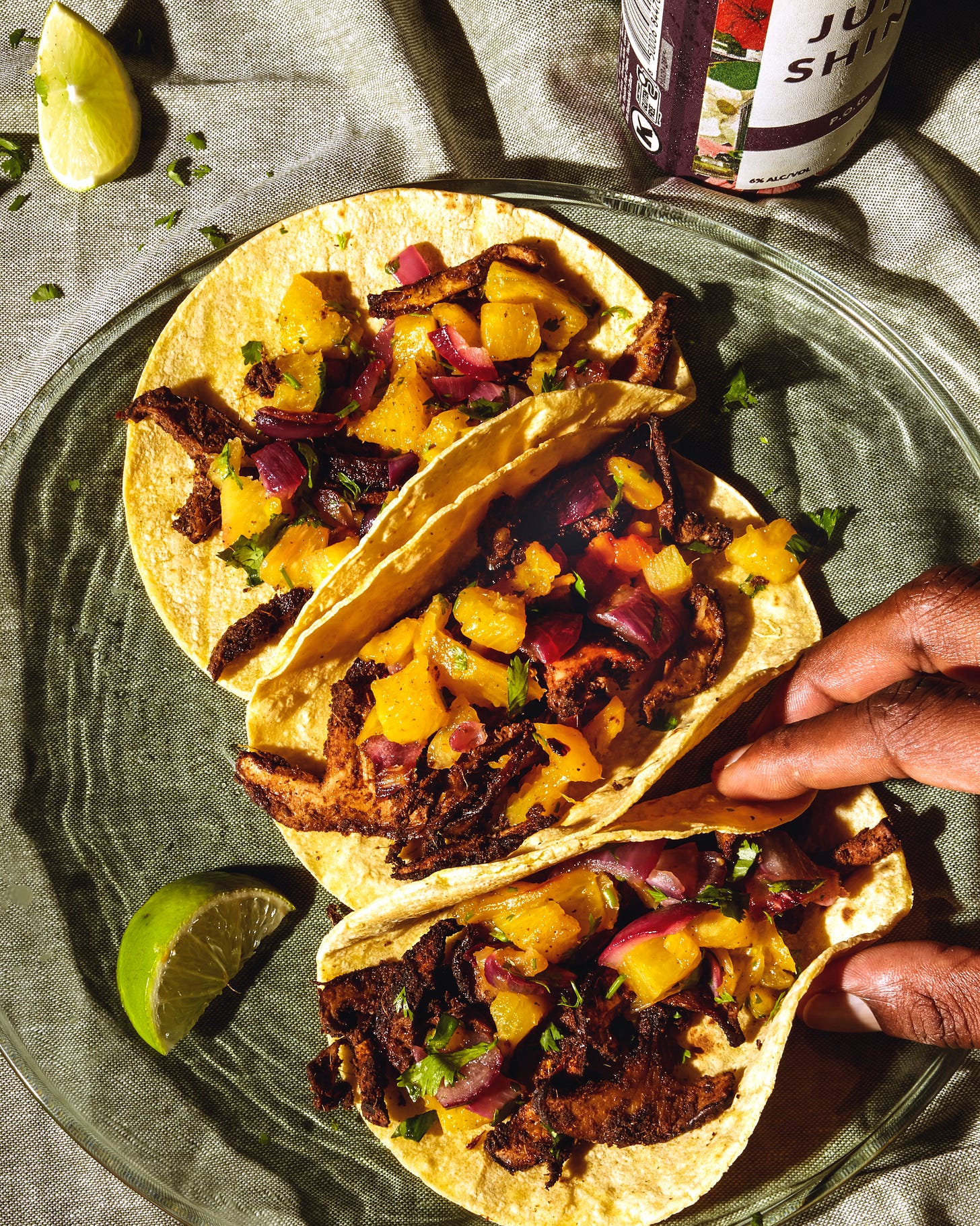 Jerk shiitake mushroom tacos on a plate with fingers grabbing one taco.