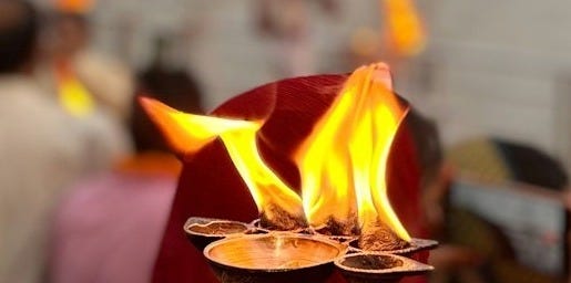 People holding lit lamps by a river at dusk.