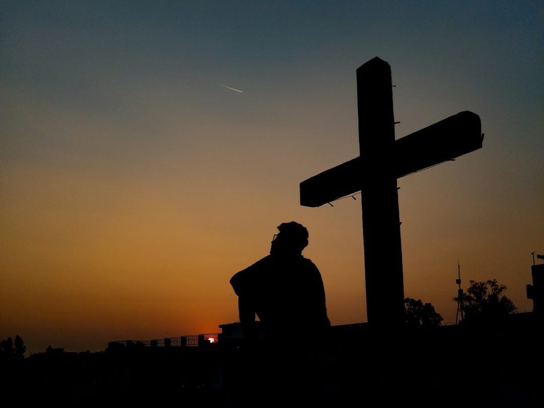 silhouette of man standing near cross during sunset