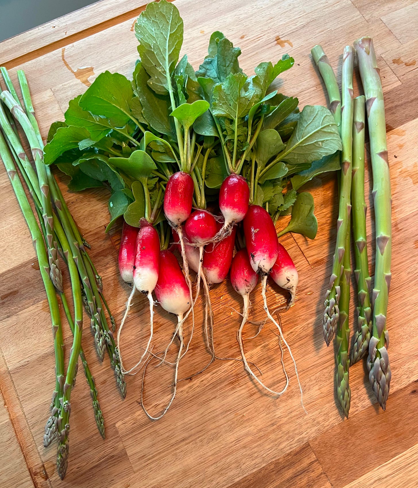 freshly harvested asparagus and radishes on a wood cutting board