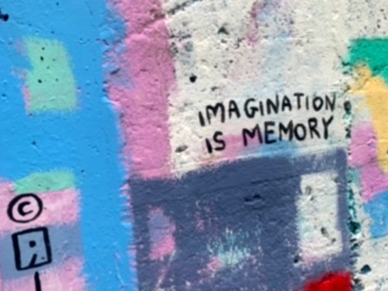 A picture of a wall with pastel paint on it in patches of blue, seafoam green, pink, white, grey, yellow, and green. In black text it says "Imagination is memory"