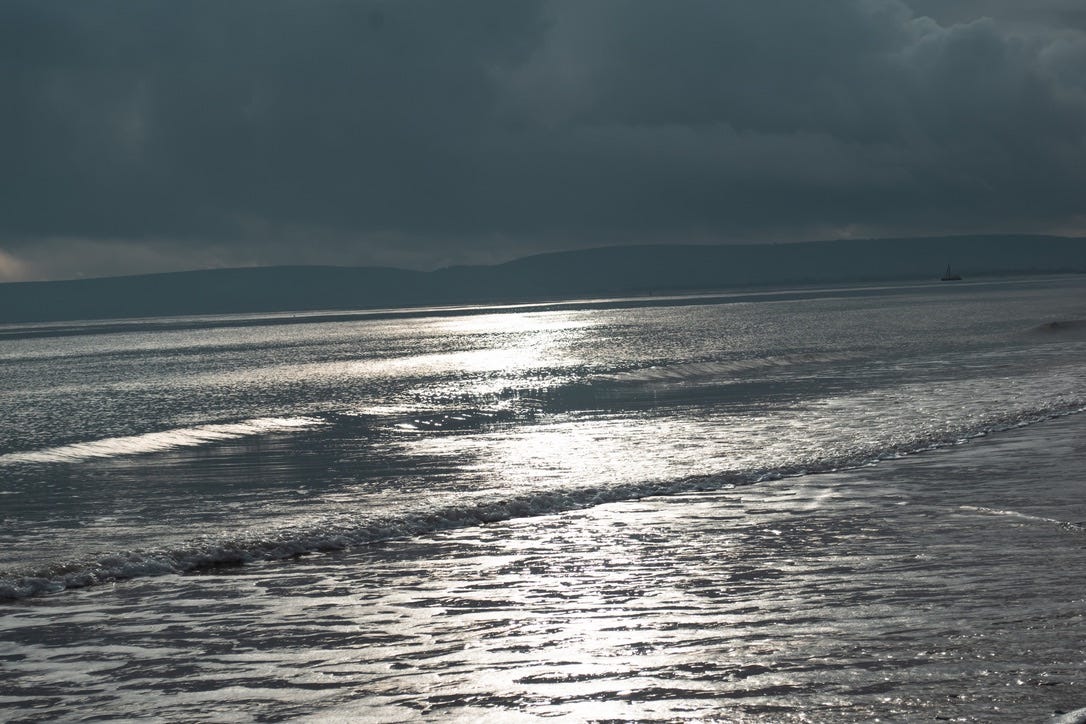 Sunlight reflecting across gentle Suffolk waves, forming a shimmering path of light on the sea beneath a soft sky.