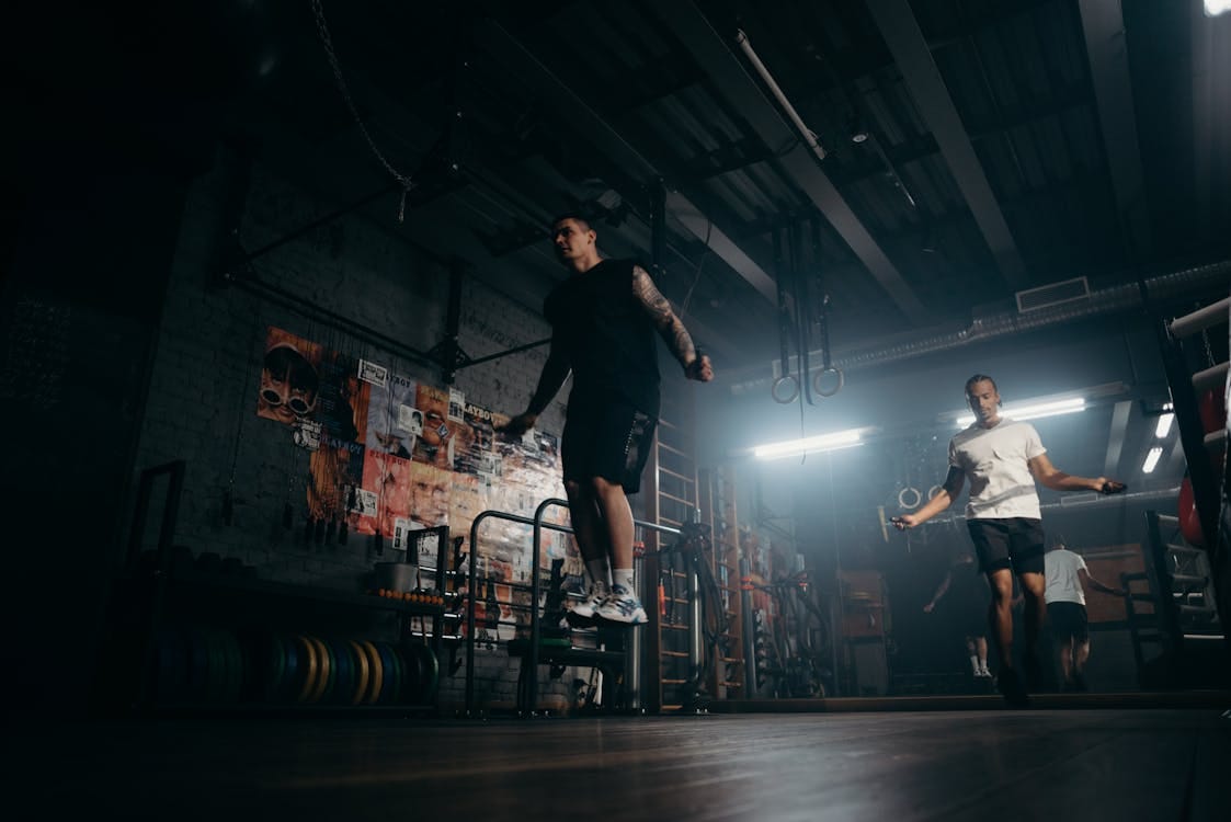 Free Two men actively skipping jump ropes in a dimly lit gym environment. Stock Photo Free Two men actively skipping jump ropes in a dimly lit gym environment. Stock Photo