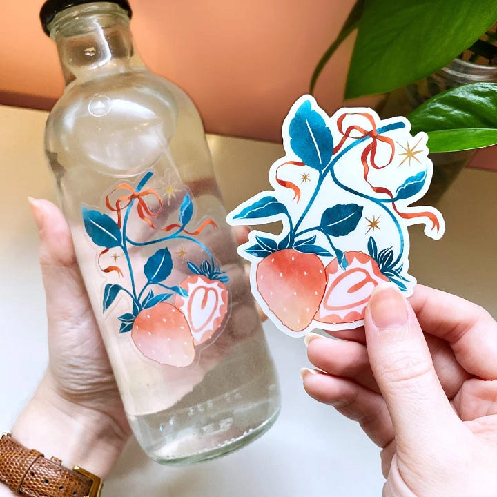 First photo: a sticker with a transparent background that features an illustration of strawberries.  Second photo: a collage print that says, "cats hate ai" with a cat laying on a computer in space.