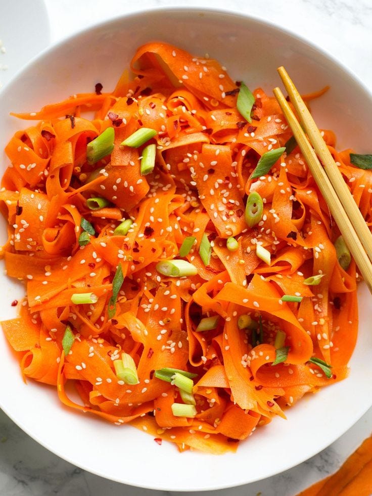 This may contain: a white bowl filled with carrot noodles and chopsticks