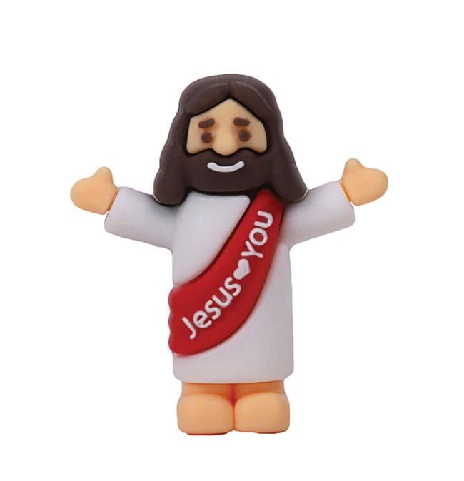 A small plastic Jesus figurine with a smiling face, brown hair and beard, a white robe, and a red sash reading “Jesus Loves You.” The figure stands with both arms outstretched in a welcoming pose against a plain white background. This is the same style of miniature plastic Jesus that eventually multiplied into fifty-four copies on the author's classroom whiteboard. A small plastic Jesus figurine with a smiling face, brown hair and beard, a white robe, and a red sash reading “Jesus Loves You.” The figure stands with both arms outstretched in a welcoming pose against a plain white background. This is the same style of miniature plastic Jesus that eventually multiplied into fifty-four copies on the author's classroom whiteboard.