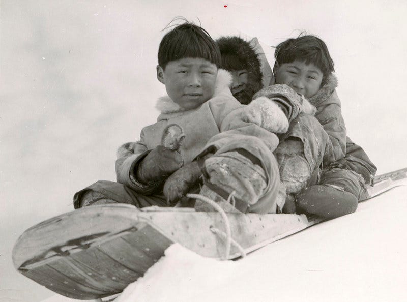Three children wearing winter furs and riding a sled. Three children wearing winter furs and riding a sled.
