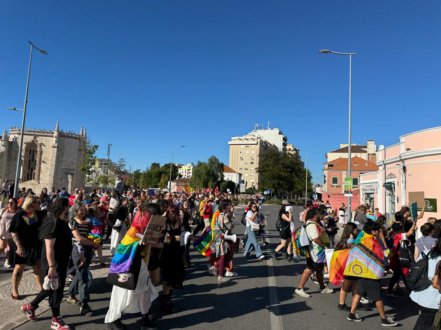 Several hundred people with rainbow flags cross a major street.