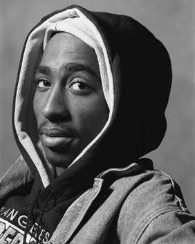A black and white photo of Tupac Shakur staring at the viewer A black and white photo of Tupac Shakur staring at the viewer