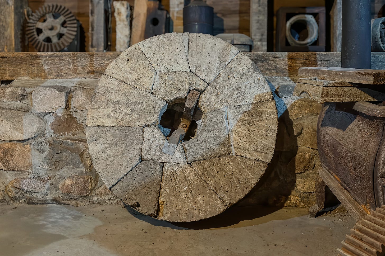 Im Innern der Bonneyville Mill im Elkhart County, Indiana, lehnt ein grosser kreisrunder Mühlstein aus hellgrauem Stein vor einer niedrigen Steinmauer. Die Oberfläche ist segmentiert und in der Mitte durchbrochen; rundherum sind weitere historische Geräte und Metallteile der alten Mühle zu sehen. Im Innern der Bonneyville Mill im Elkhart County, Indiana, lehnt ein grosser kreisrunder Mühlstein aus hellgrauem Stein vor einer niedrigen Steinmauer. Die Oberfläche ist segmentiert und in der Mitte durchbrochen; rundherum sind weitere historische Geräte und Metallteile der alten Mühle zu sehen.