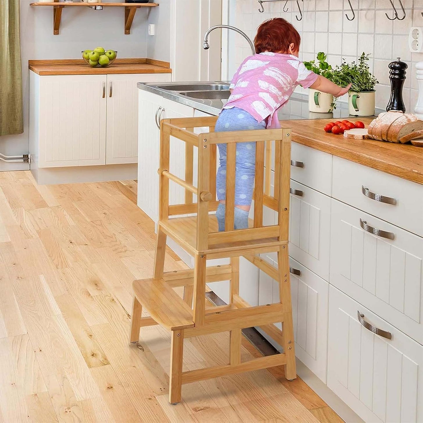 young child stands on a wooden stairstool to reach a kitchen counter