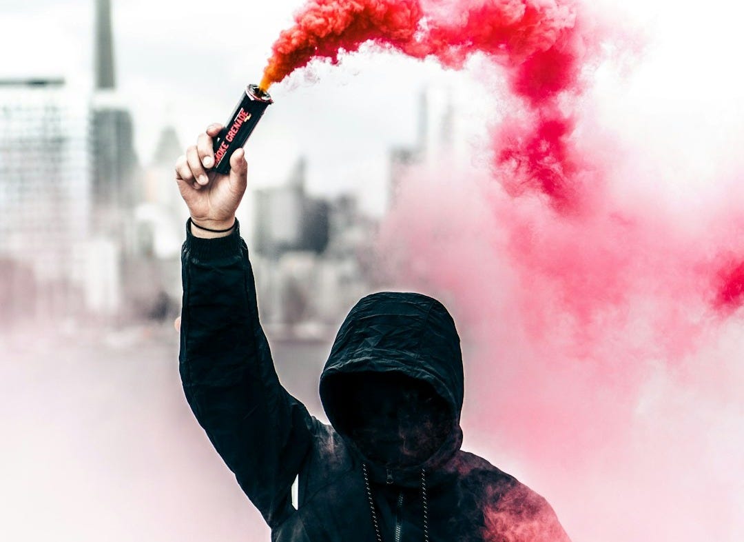 person wearing black and red hoodie holding smoke bomb