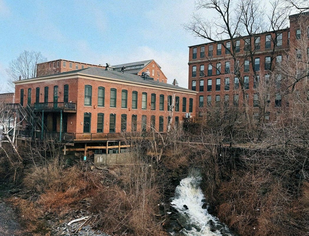 Brick buildings sit beside a rushing river.