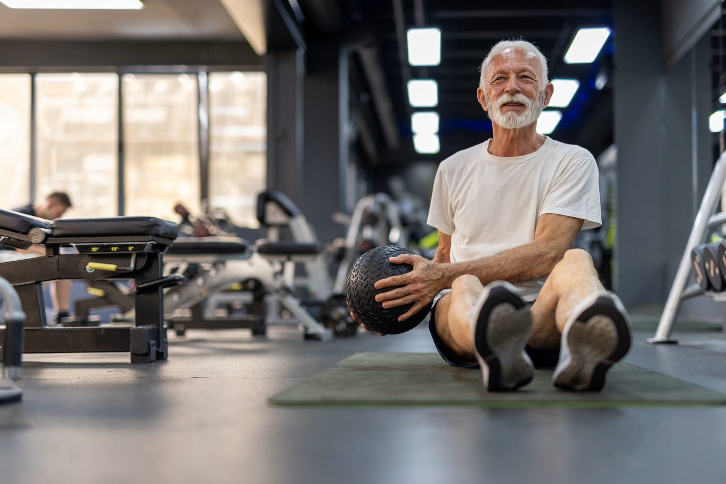 Older man in a gym doing Russian twists with a weighted ball. Older man in a gym doing Russian twists with a weighted ball.