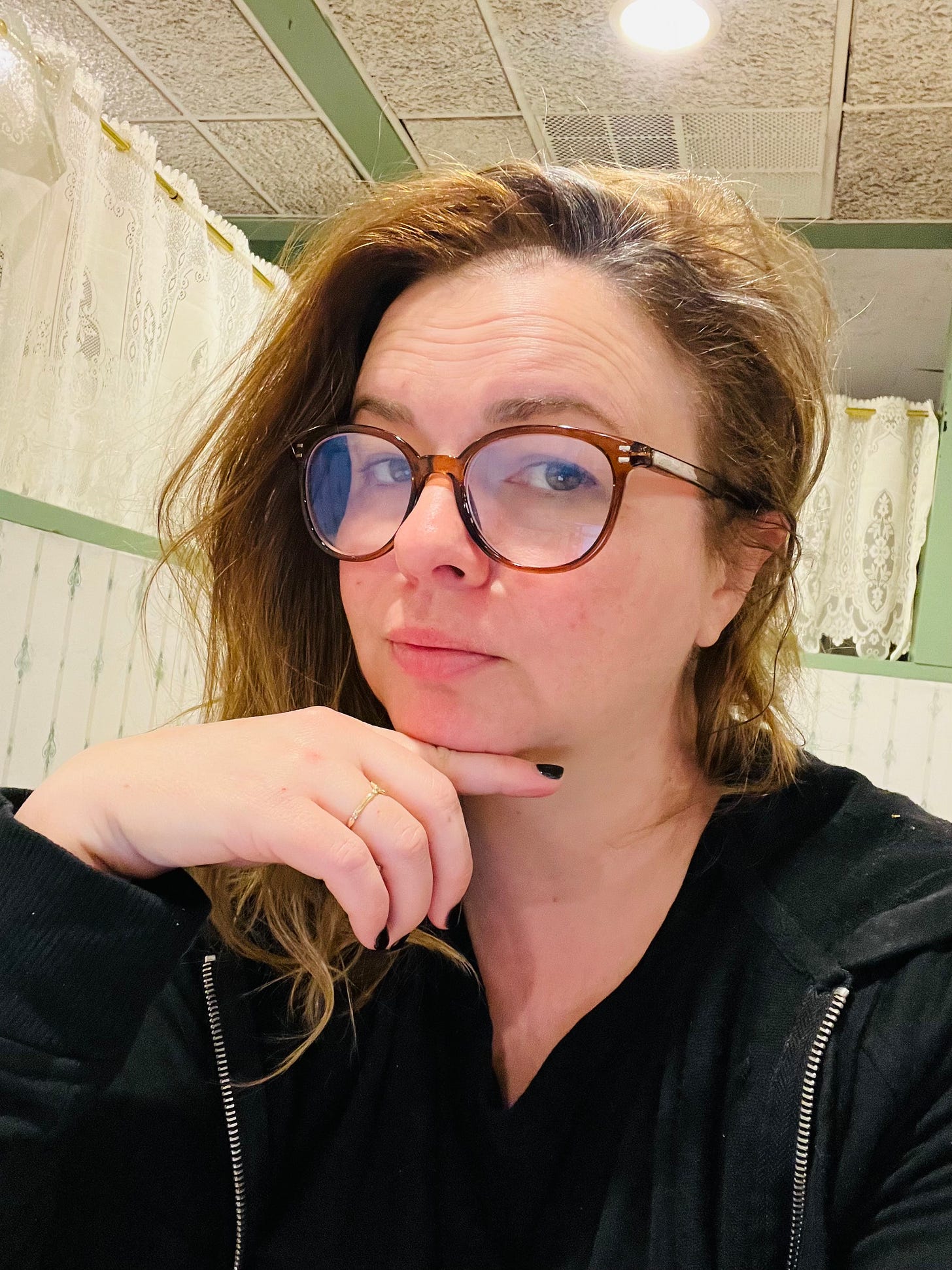 A selfie of Amber. She wears a black hoodie and reading glasses.