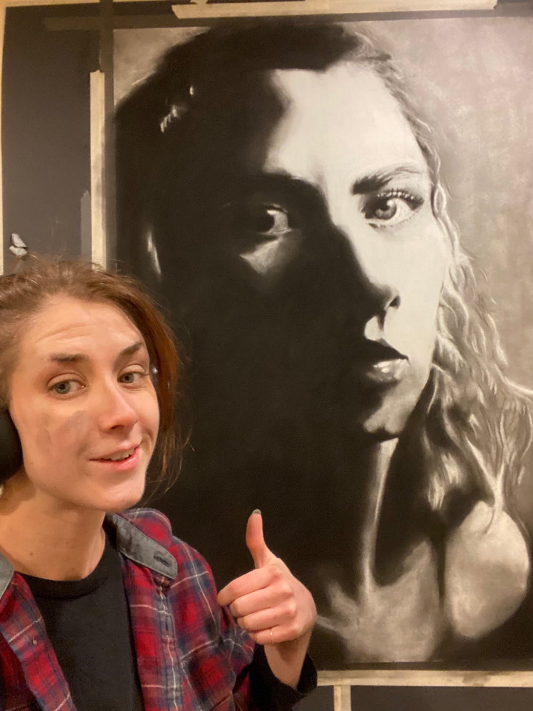young woman giving thumbs up sign while standing in front of large charcoal drawing self portrait work in progress young woman giving thumbs up sign while standing in front of large charcoal drawing self portrait work in progress
