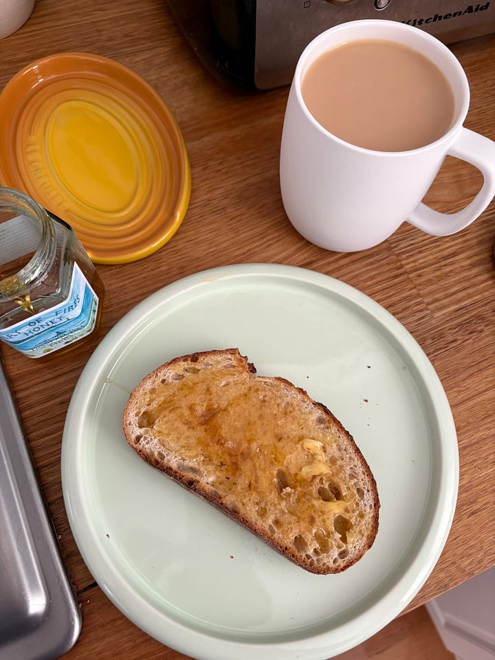 A slice of toast with butter, honey and tea. A matcha latte on a dining table with breakfast in the background