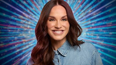 Vicky Pattison smiles for the camera wearing a blue denim shirt, set against a glittering blue background