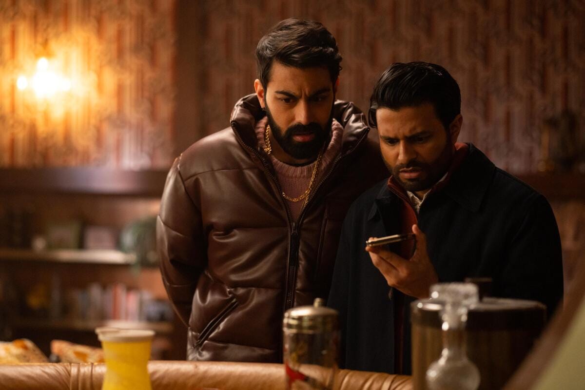 Two men in coats with frowning faces look at a phone.