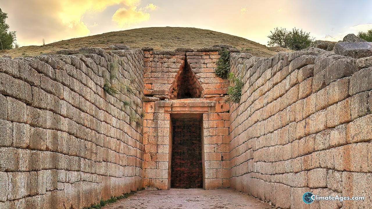 A stone-lined passage leads to the dark entrance of the Treasury of Atreus at Mycenae, beneath a triangular opening and a dry hillside.
