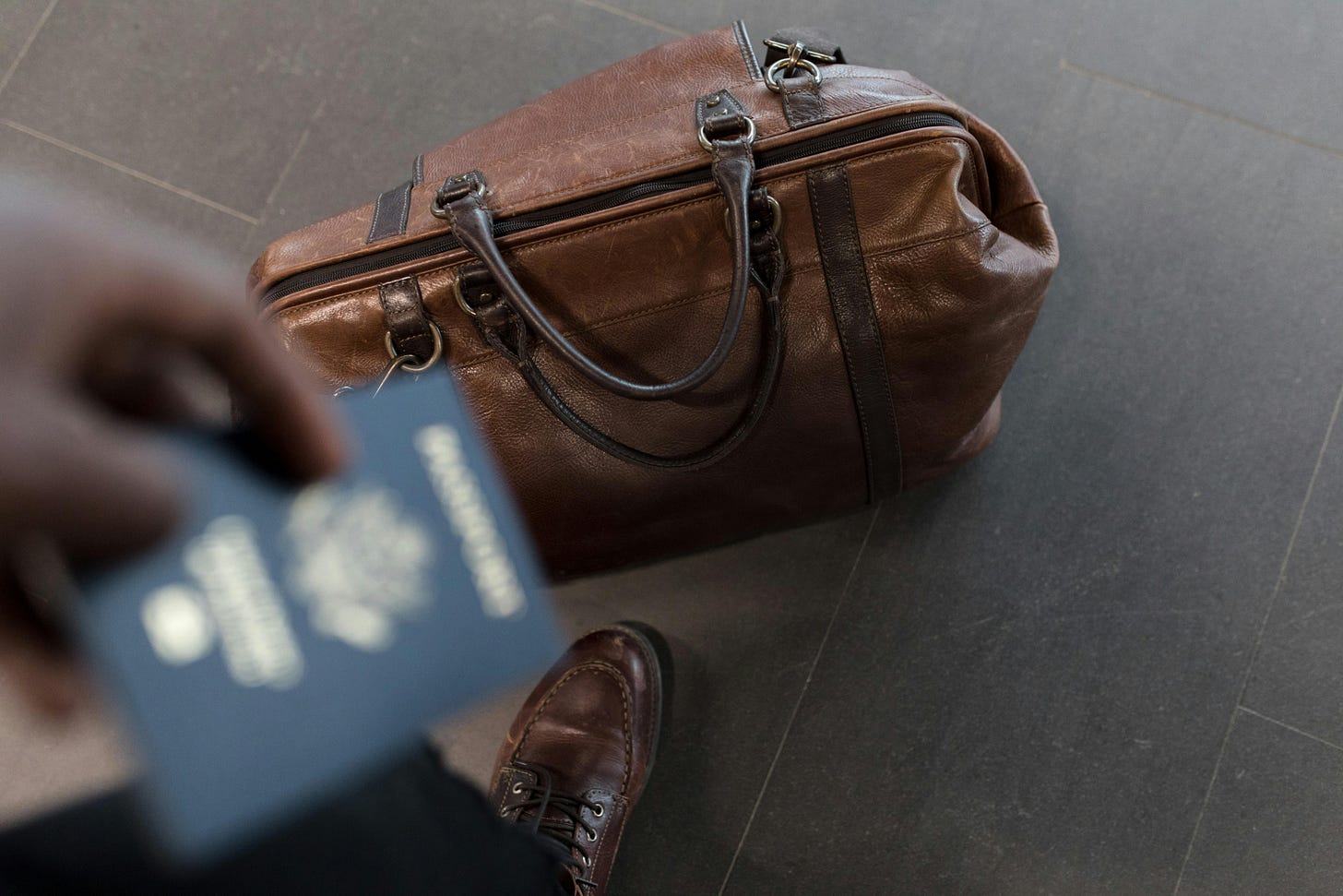 Brown leather duffel bag on floor with passport in foreground Brown leather duffel bag on floor with passport in foreground