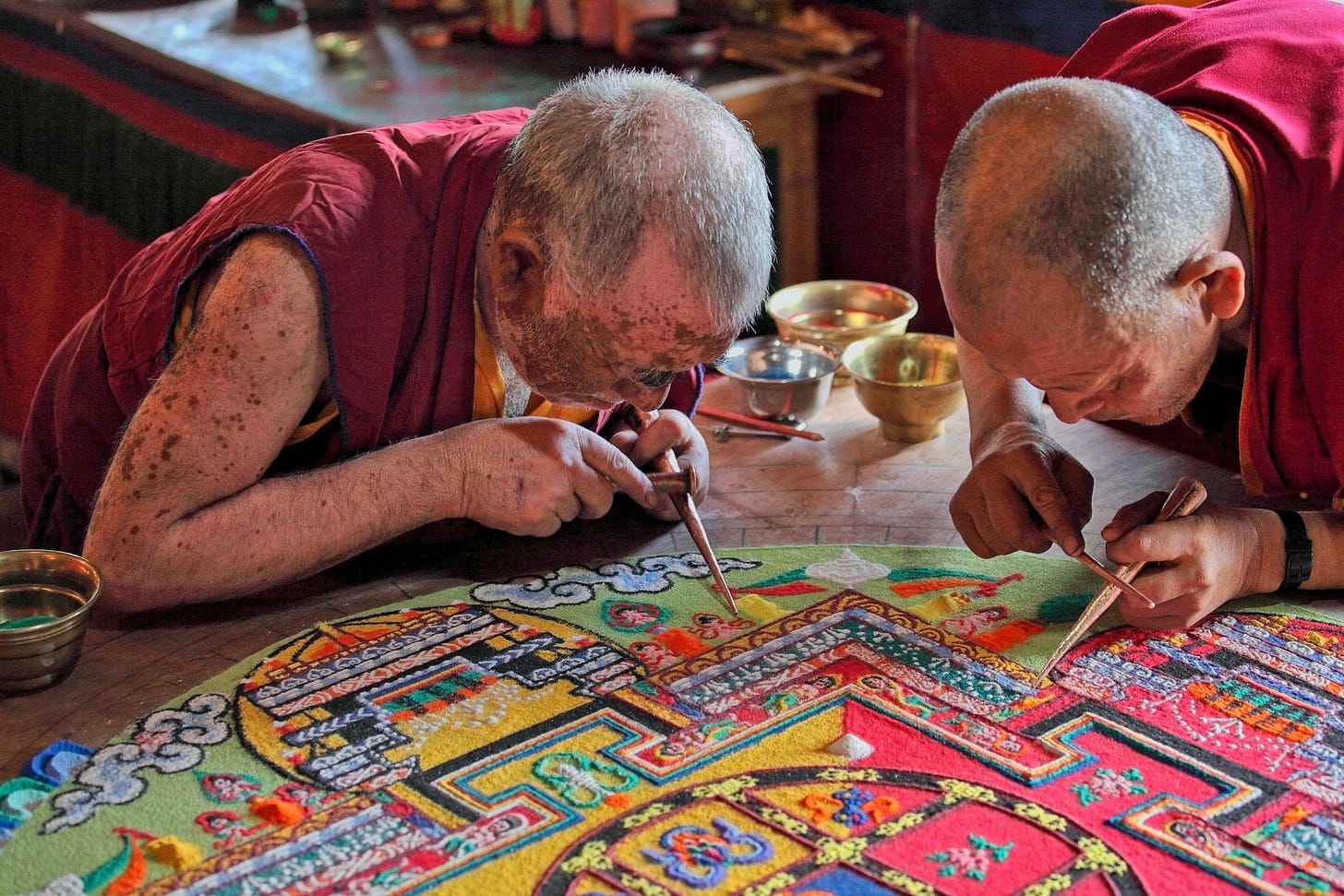Two monks work intently with pointed sticks on a sand mandala