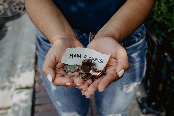 A woman holds a handful of coins, and a small note that reads: “Make a change.” A woman holds a handful of coins, and a small note that reads: “Make a change.”