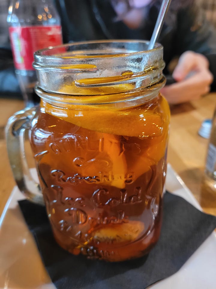 On the right, a plate of potato pancakes with a side of goulash; on the left, a glass of herbal tea in a mason jar.