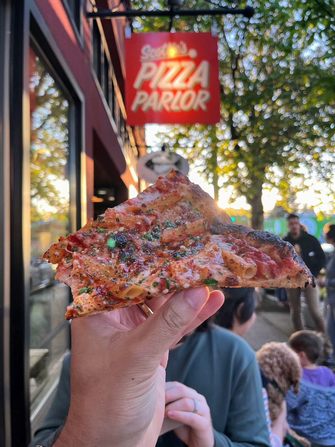 Hand holding half eaten So What, No F*ckin' Ziti Now?! pizza slice
