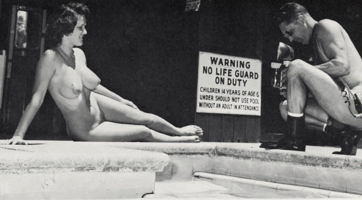 Black-and-white photograph from 1963 showing a nude woman seated at the edge of a swimming pool while a clothed male photographer kneels nearby with a camera aimed toward her. A posted sign behind them reads, “Warning: No lifeguard on duty,” with additional text about children and pool use. The setting appears informal and candid rather than studio-staged. Black-and-white photograph from 1963 showing a nude woman seated at the edge of a swimming pool while a clothed male photographer kneels nearby with a camera aimed toward her. A posted sign behind them reads, “Warning: No lifeguard on duty,” with additional text about children and pool use. The setting appears informal and candid rather than studio-staged.