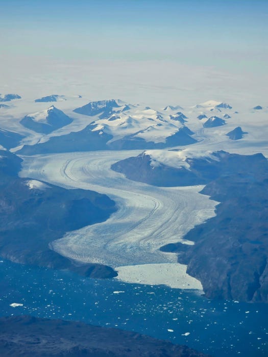 Aerial view of massive glacier flowing through mountain valley into ocean Aerial view of massive glacier flowing through mountain valley into ocean