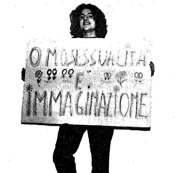 Grainy scan of a photo of a smiling person with long dark hair holding a placard decorated with flowers and double venus/mars symbols, which reads, OMOSESSUALITA E IMMAGINAZIONE