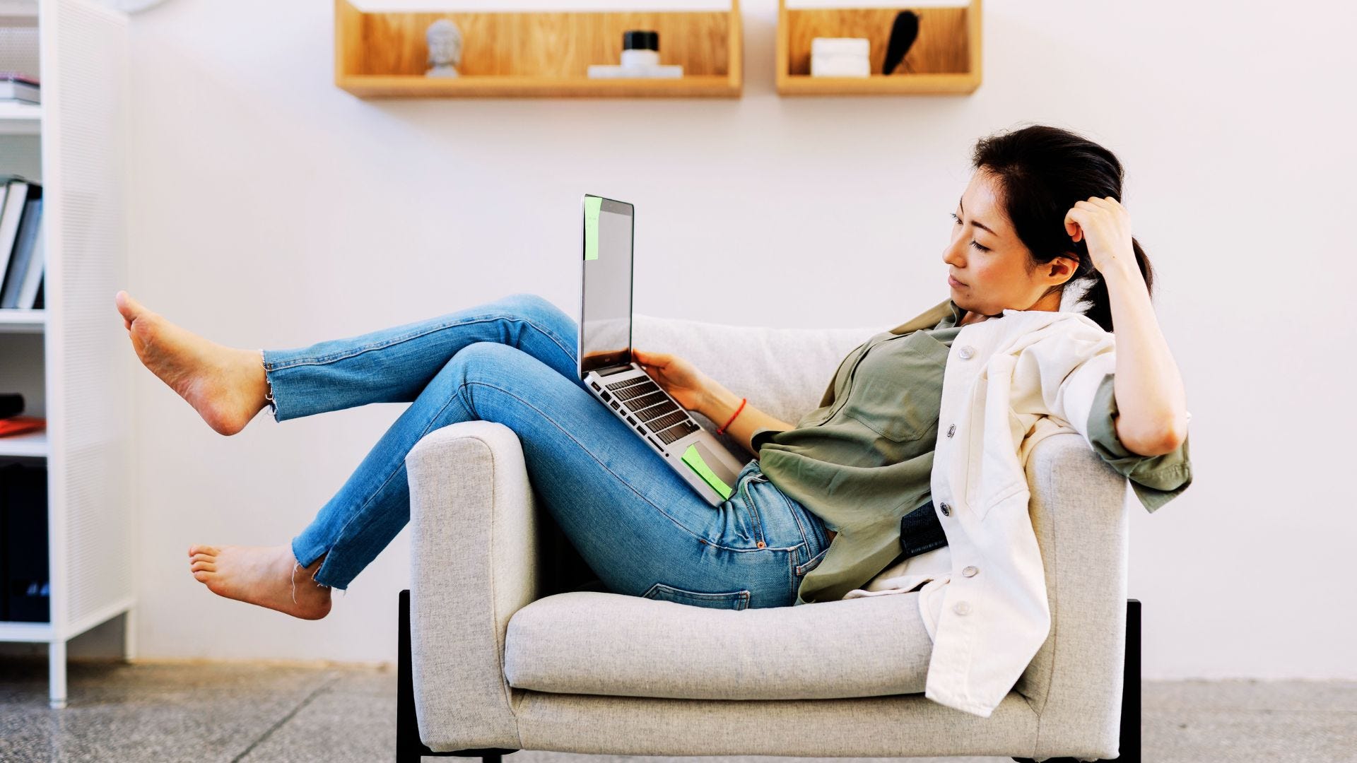 young asian woman is stretched out on a chair while looking at her laptop