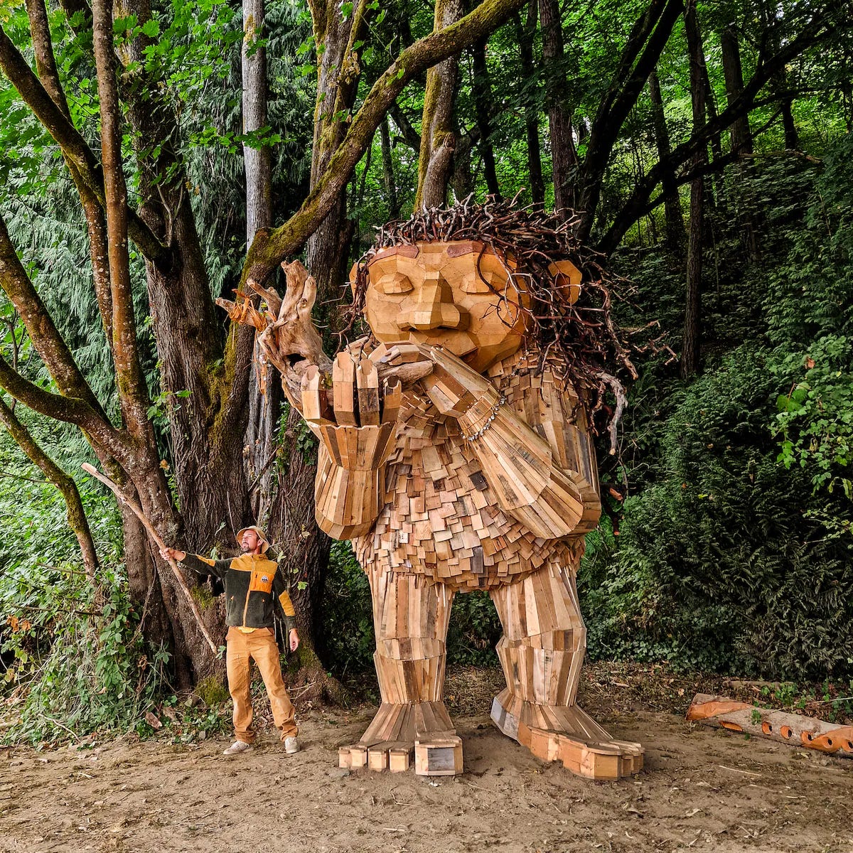 A person standing next to a statue of a person in a forest

Description automatically generated