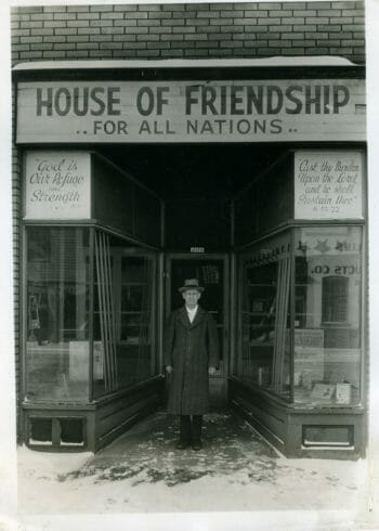Black and white image with a man standing in front of a storefront with a sign above the door that says "House of Friendship for All Nations".