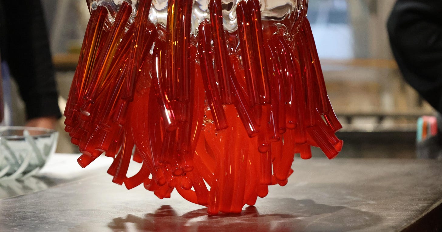A glass vessel of red and orange canes hanging from a clear shell, on a workbench in a Murano furnace A glass vessel of red and orange canes hanging from a clear shell, on a workbench in a Murano furnace