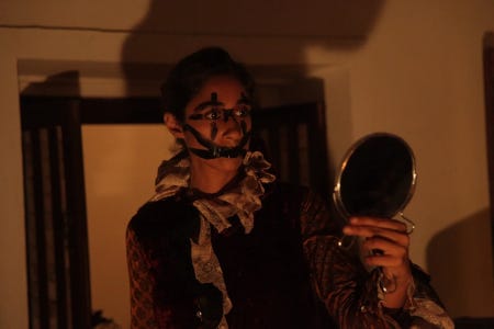 L'artiste au visage maquillé de noir s'observe dans un miroir de poche, dans un appartement sombre L'artiste au visage maquillé de noir s'observe dans un miroir de poche, dans un appartement sombre